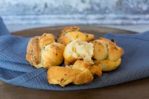 Vegan garlic knots with green garnish on blue kitchen towel and plate.