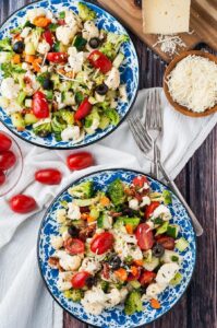 Two plates filled with vegetable salad with broccoli, cauliflower, tomatoes and olives on table.