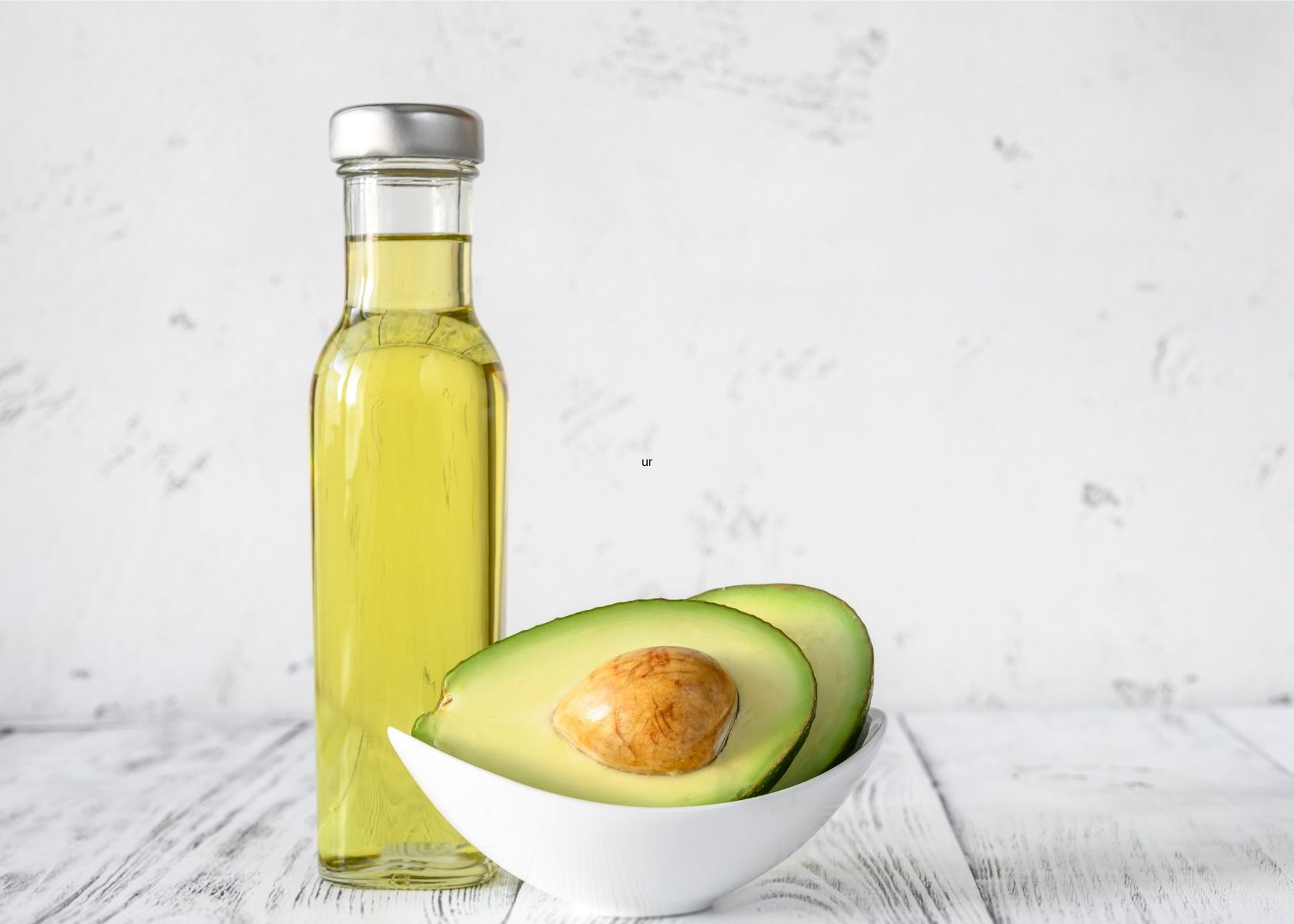 Avocado oil in glass bottle next to white bowl of cut avocados.
