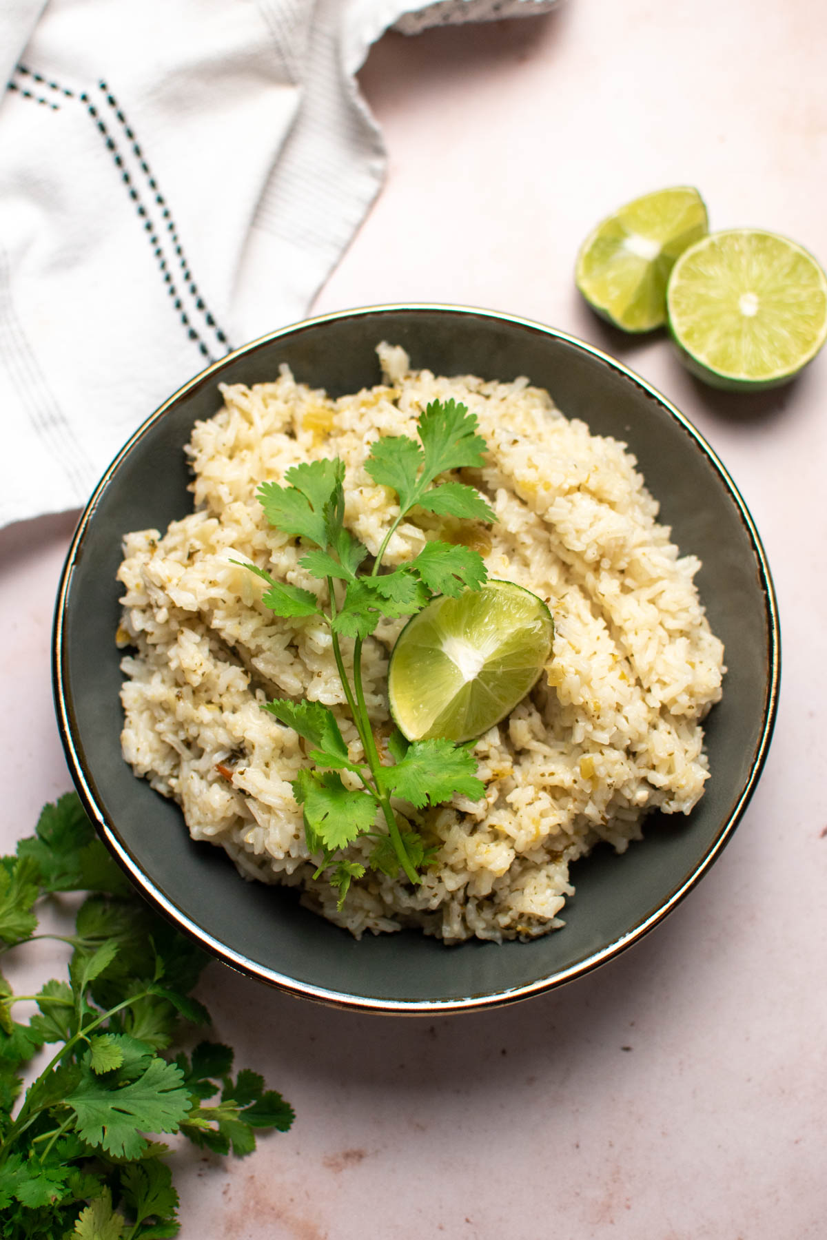 Gray bowl of cilantro lime rice on table with limes and fresh cilantro nearby.