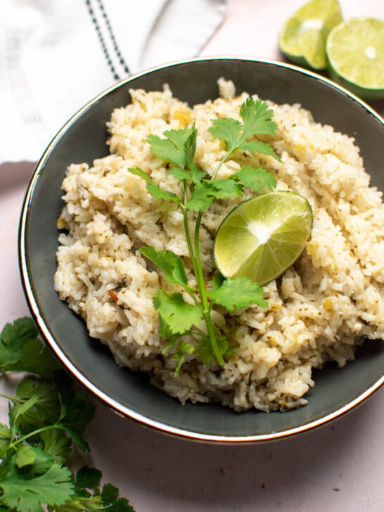 Cilantro lime rice in gray bowl on table with towel and cut lime.