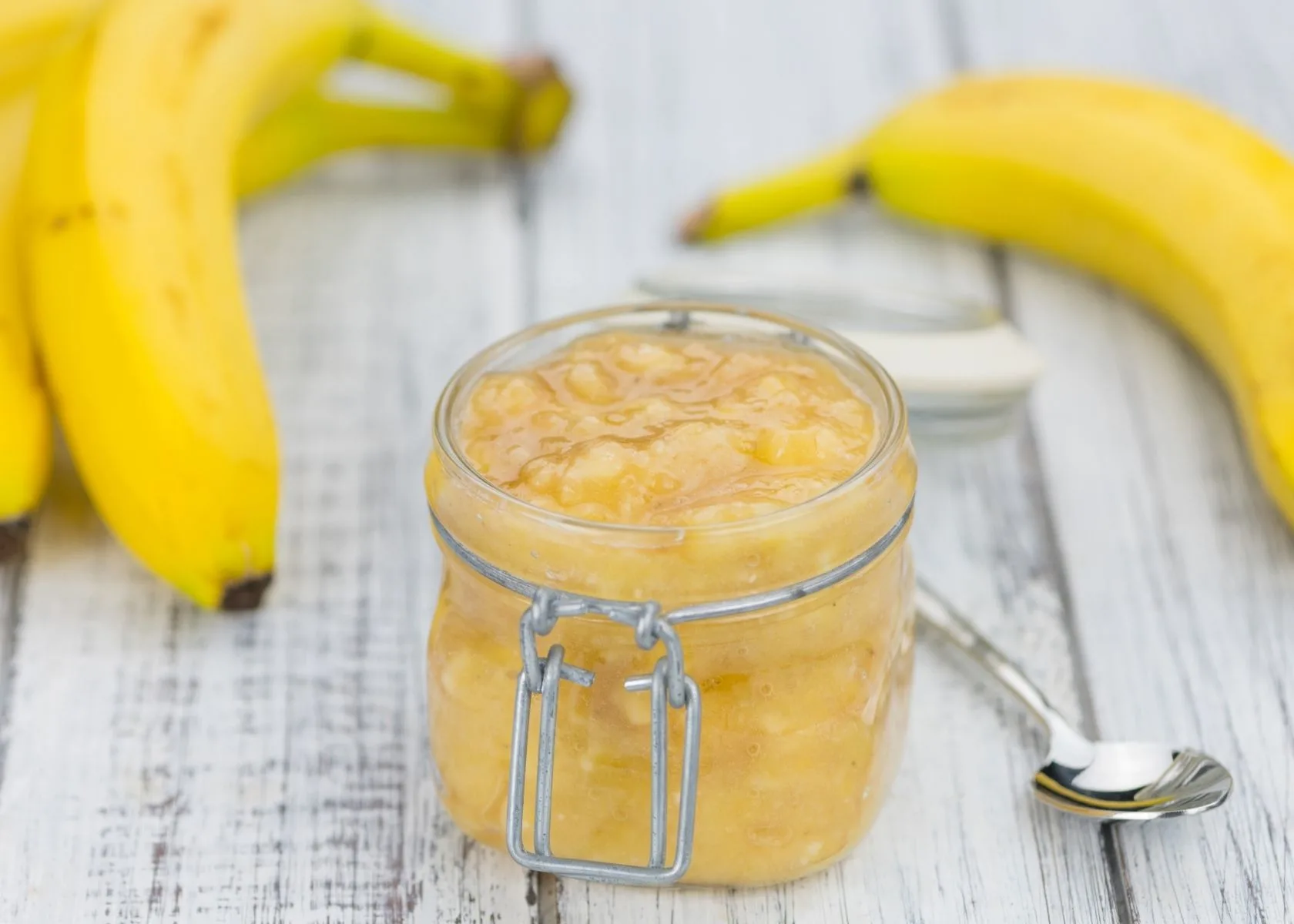 Mashed banana butter substitute in glass jar next to fresh bananas and spoon.