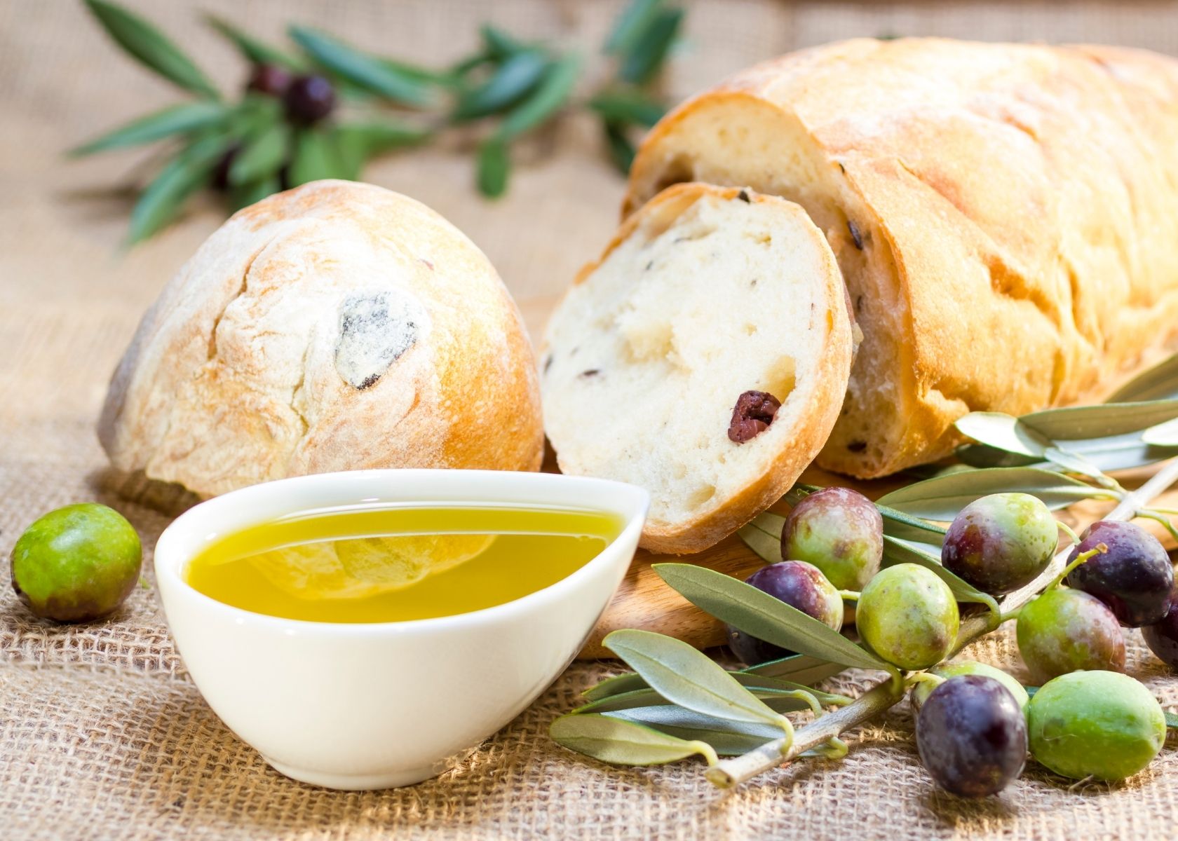 Olive oil next to crusty rustic bread with whole green and purple olives.