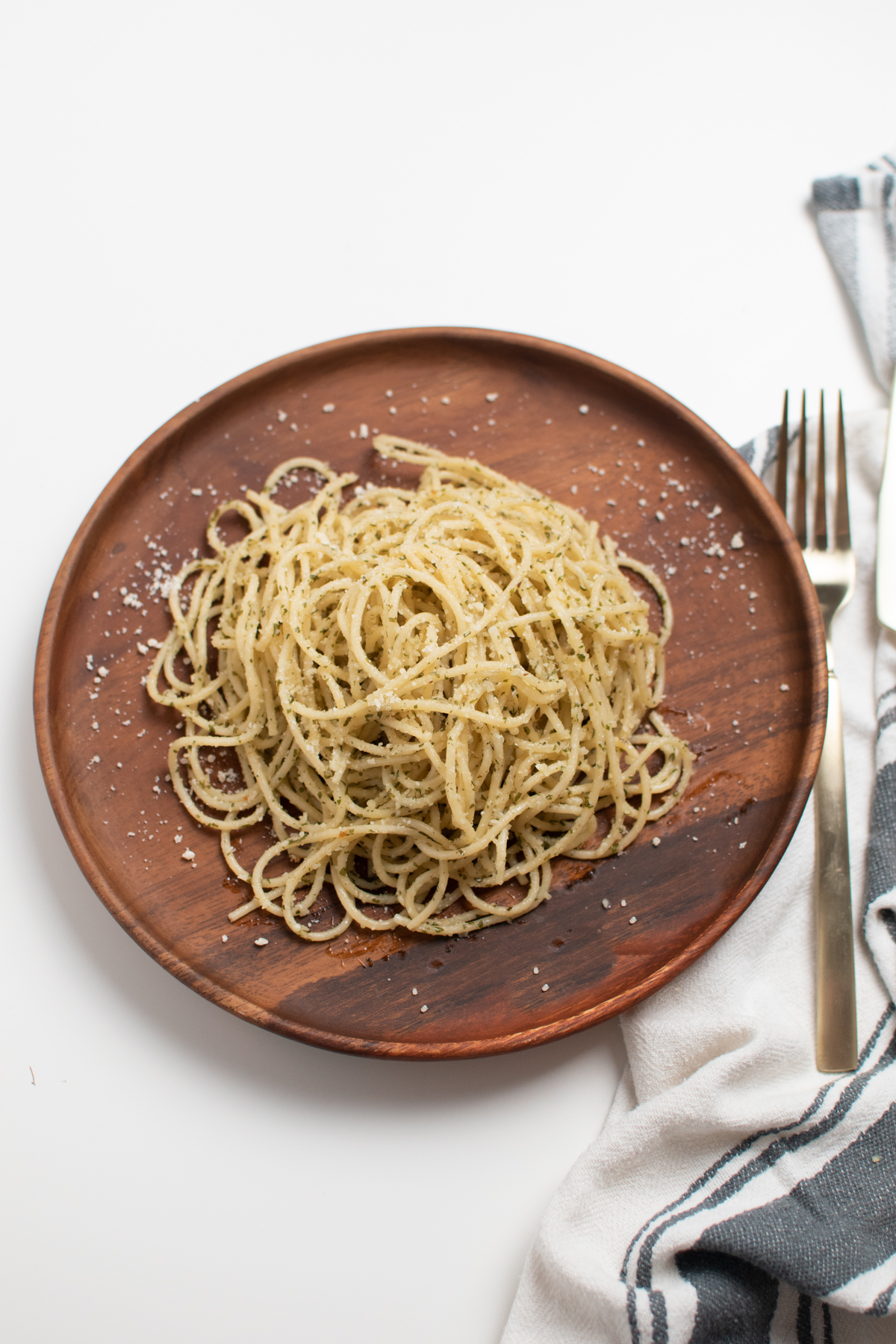 Aglio olio recipe on wood plate next to fork and gray and white kitchen towel.