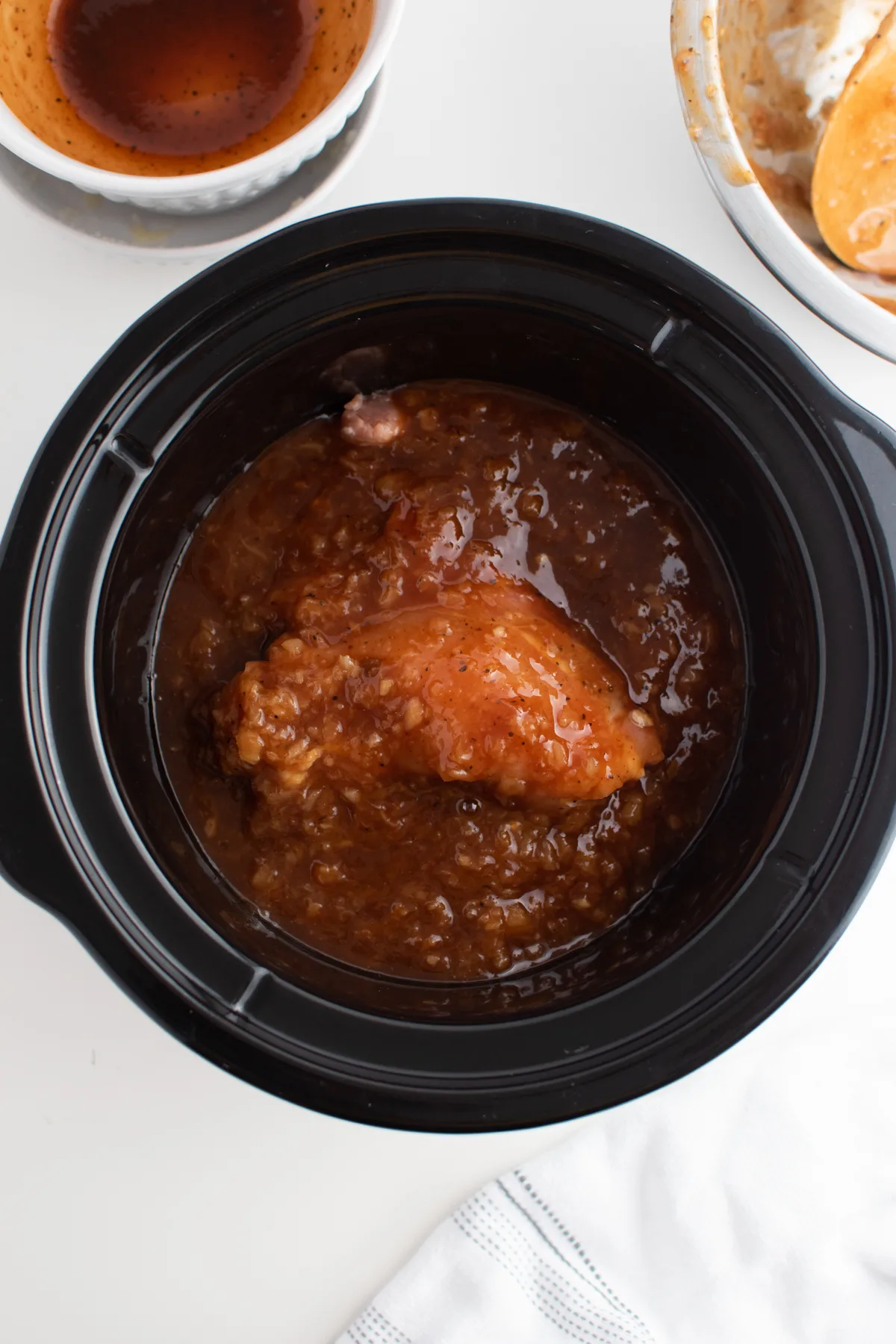 Cooked BBQ chicken thighs in large black Crock Pot with lots of sauce.