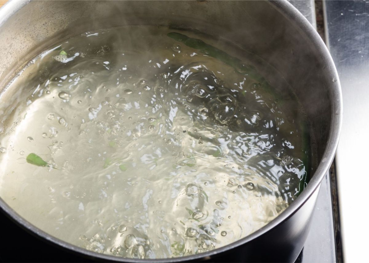 Boiling water in a large metal stock pot with green leaves inside.