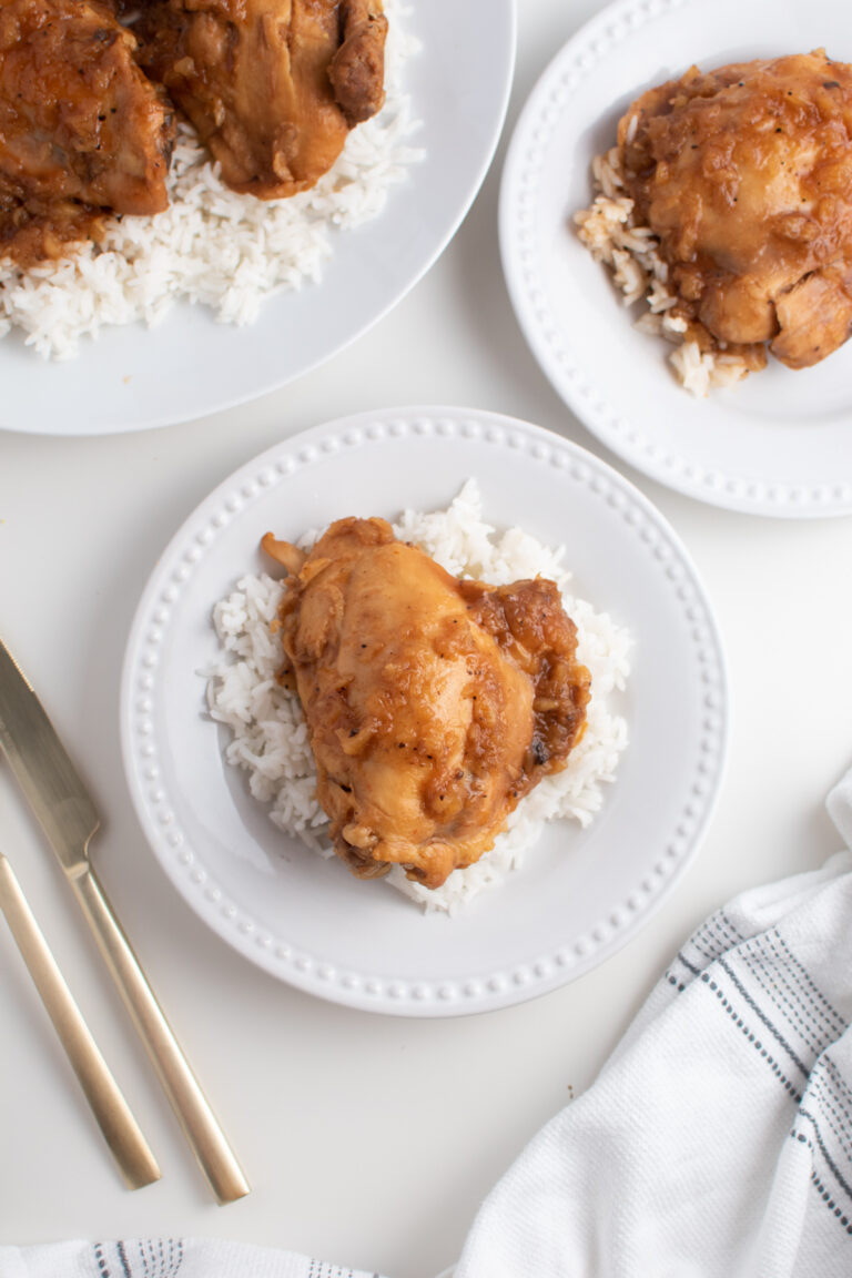 Crock Pot BBQ chicken thighs over rice with sauce on white dinner plates.