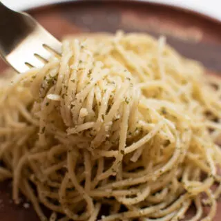 Close up of forkful of garlic spaghetti specked with basil lifted from wooden plate.