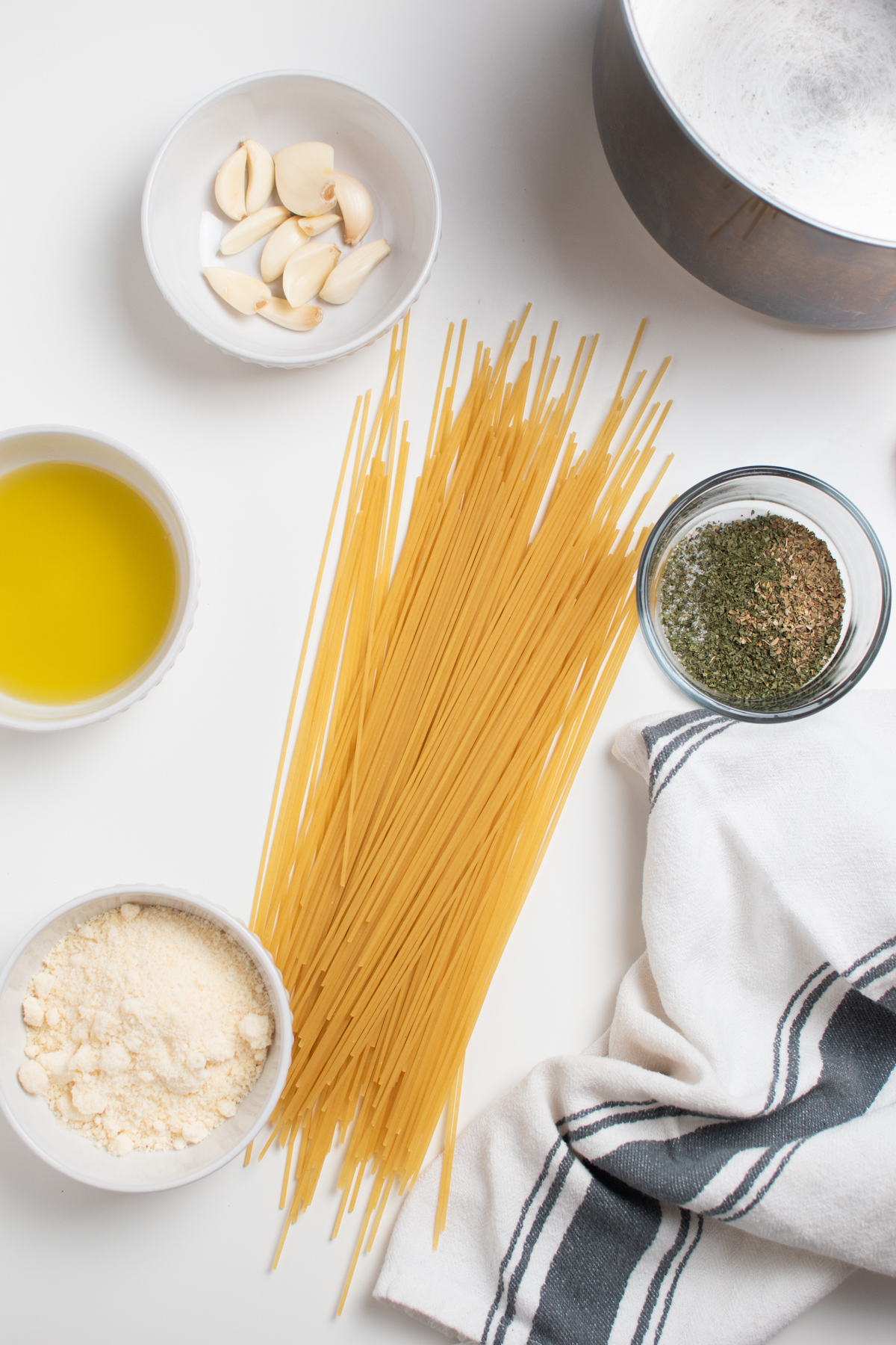 Garlic spaghetti ingredients including dry pasta, garlic, Italian seasoning, parmesan and oil.