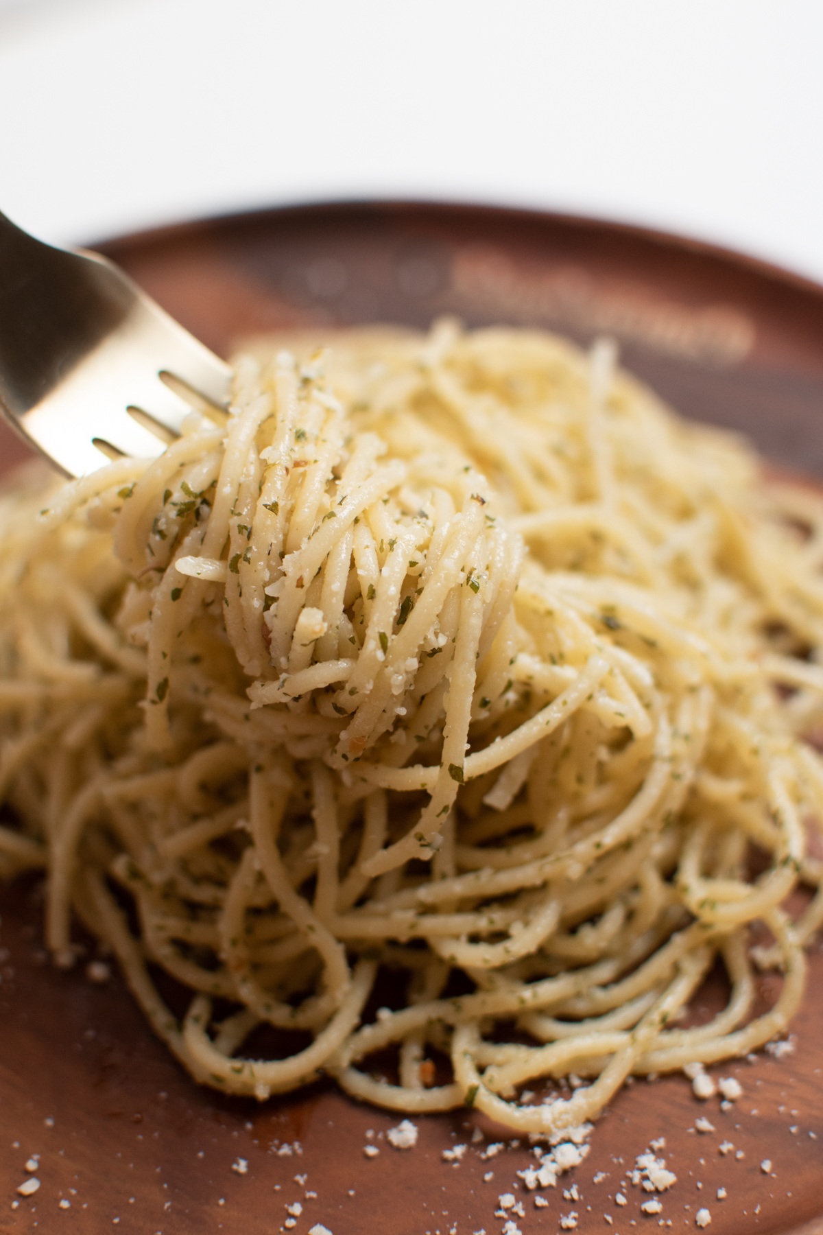 Forkful of cooked garlic spaghetti with Italian seasonings and parmesan on wooden plate.
