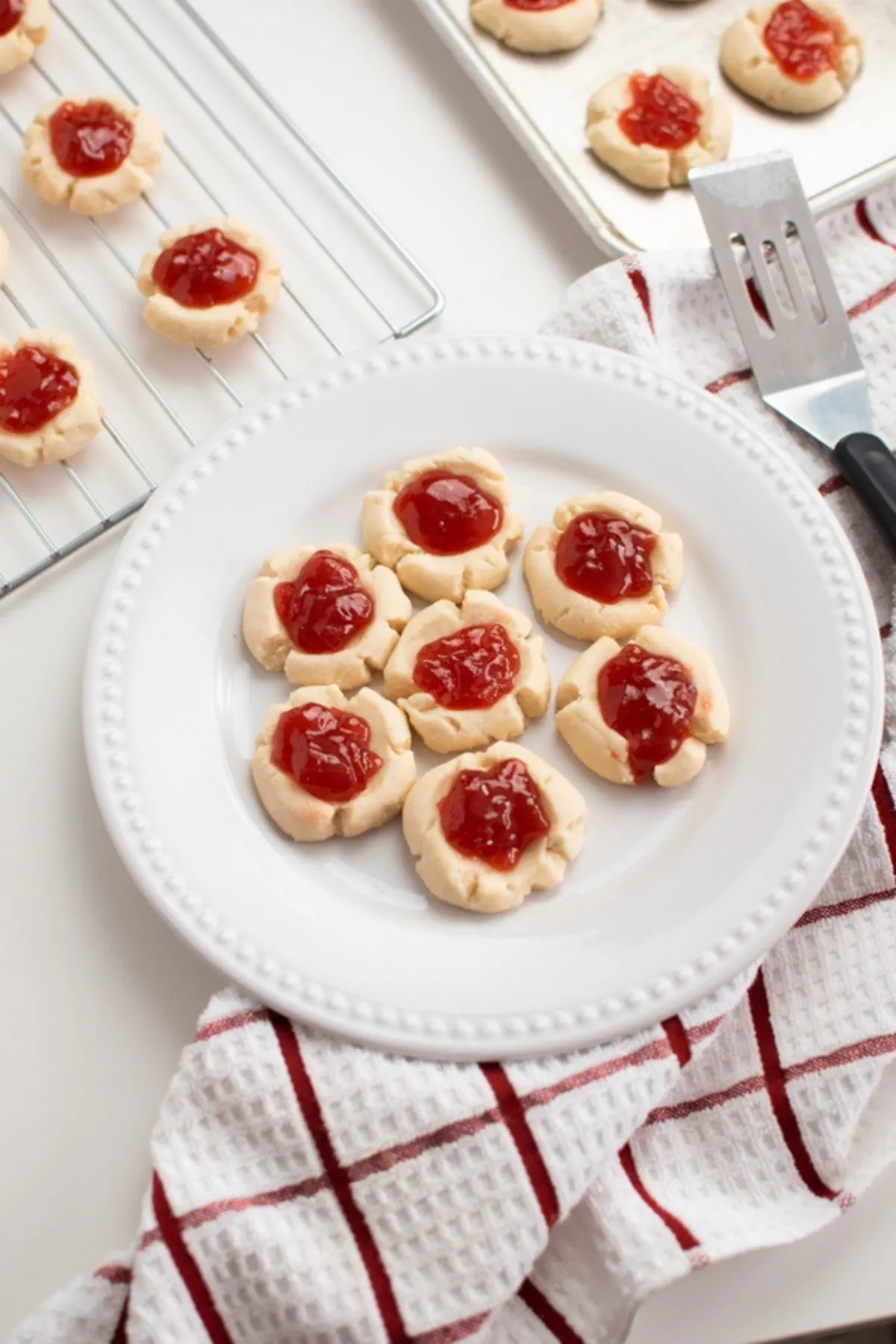 Thumbprint cookies on a white plate, cooling rack and metal baking pan.