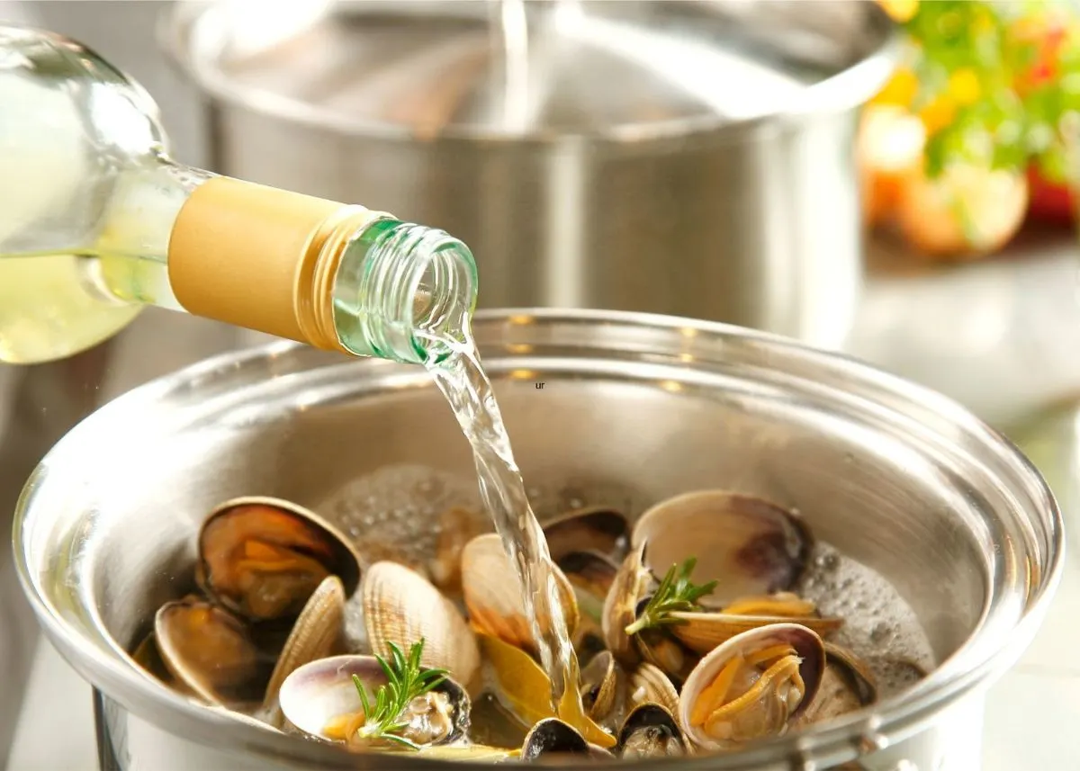 White wine poured out of clear bottle into pot of clams.