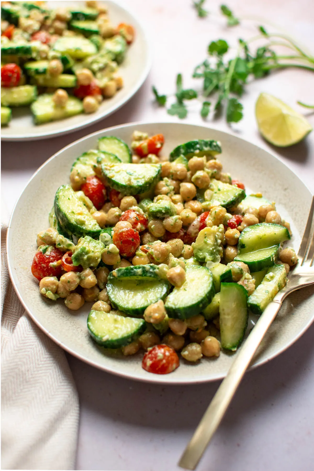 Fork rests on plate of cilantro chickpea salad with tomatoes and cucumbers.
