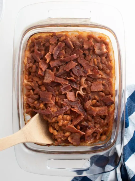 Glass casserole baking dish with baked beans with bacon and kitchen towel.