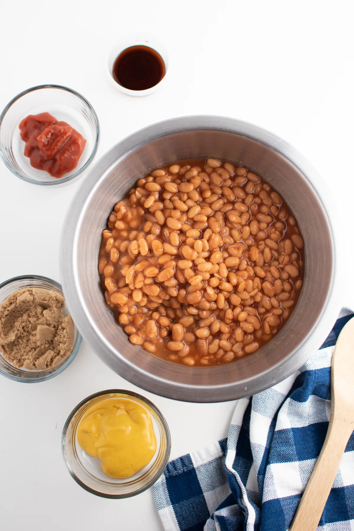 Baked beans, ketchup, brown sugar and mustard in mixing bowls on kitchen counter.