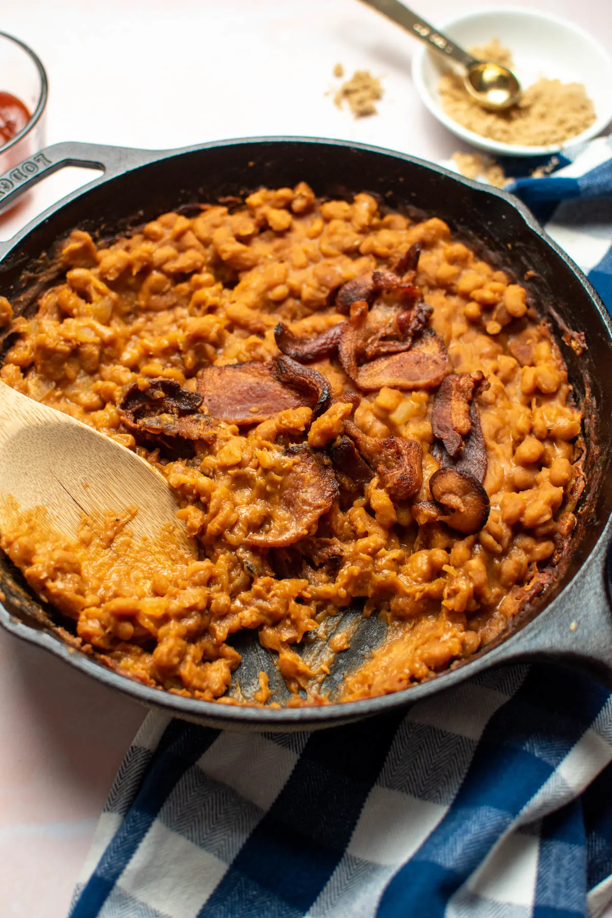 Wooden spoon resting in cast iron skillet of baked beans with mustard and brown sugar.
