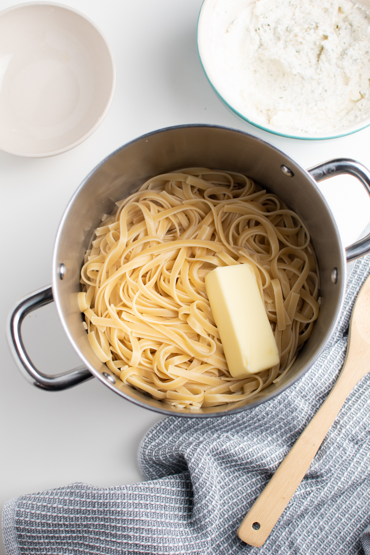 Stick of butter on cooked fettuccini noodles inside large metal stock pot.