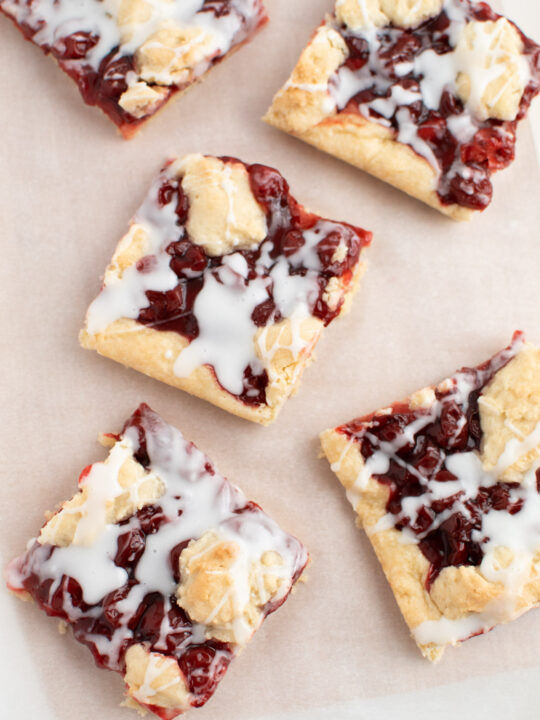 Several cherry bars cut into squares on light brown parchment paper with white frosting.
