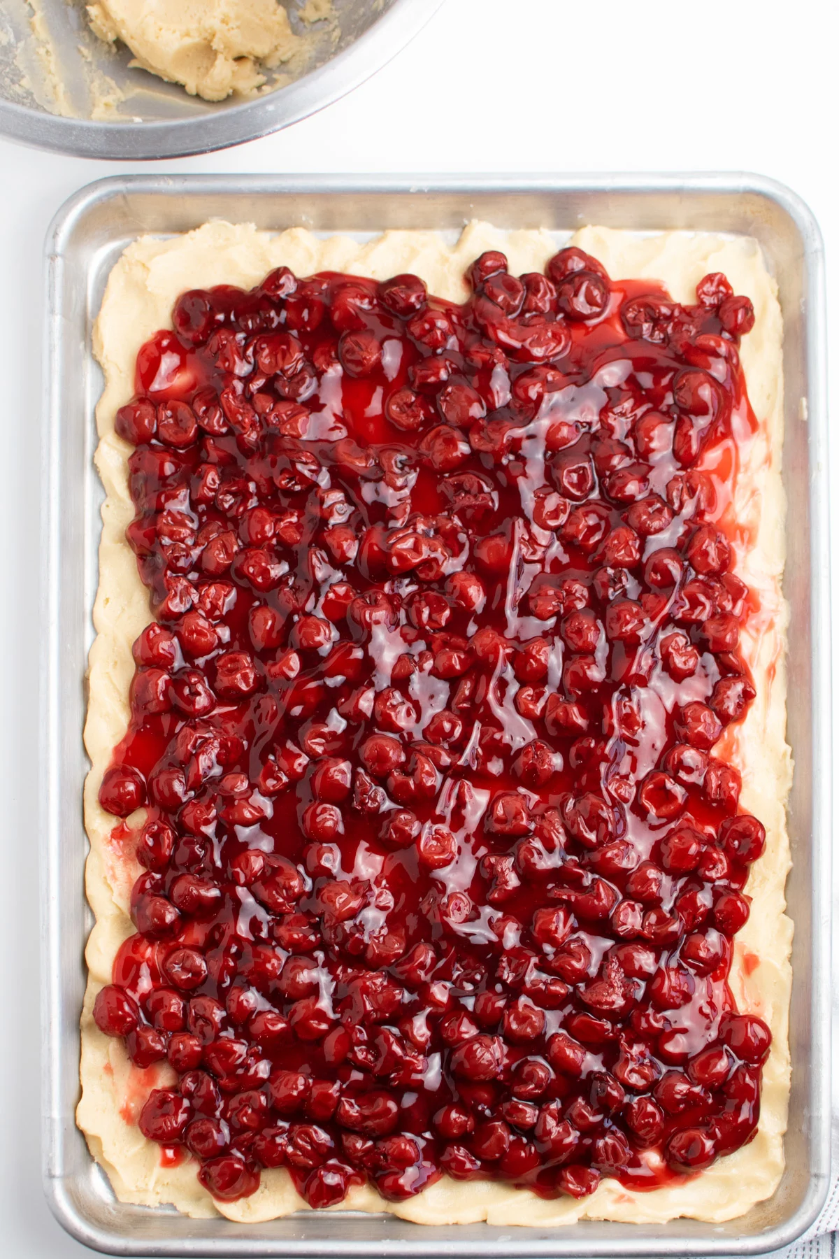Cherry pie filling spread over shortbread crust on large metal baking sheet.