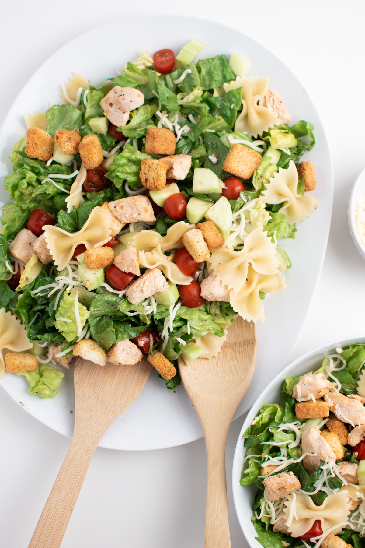 Chicken Caesar salad with pasta, croutons, cheese and tomatoes on white platter.