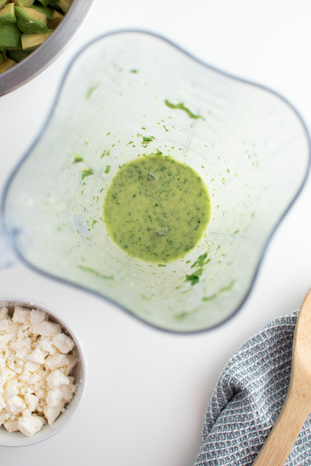 Cilantro lime dressing in blender next to bowl of feta and blue kitchen towel.