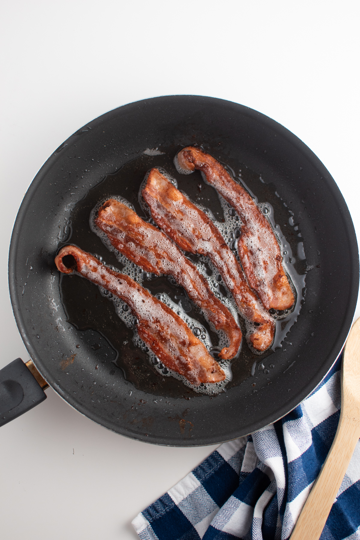 4 strips of cooked bacon in small black frying pan with bubbling grease.