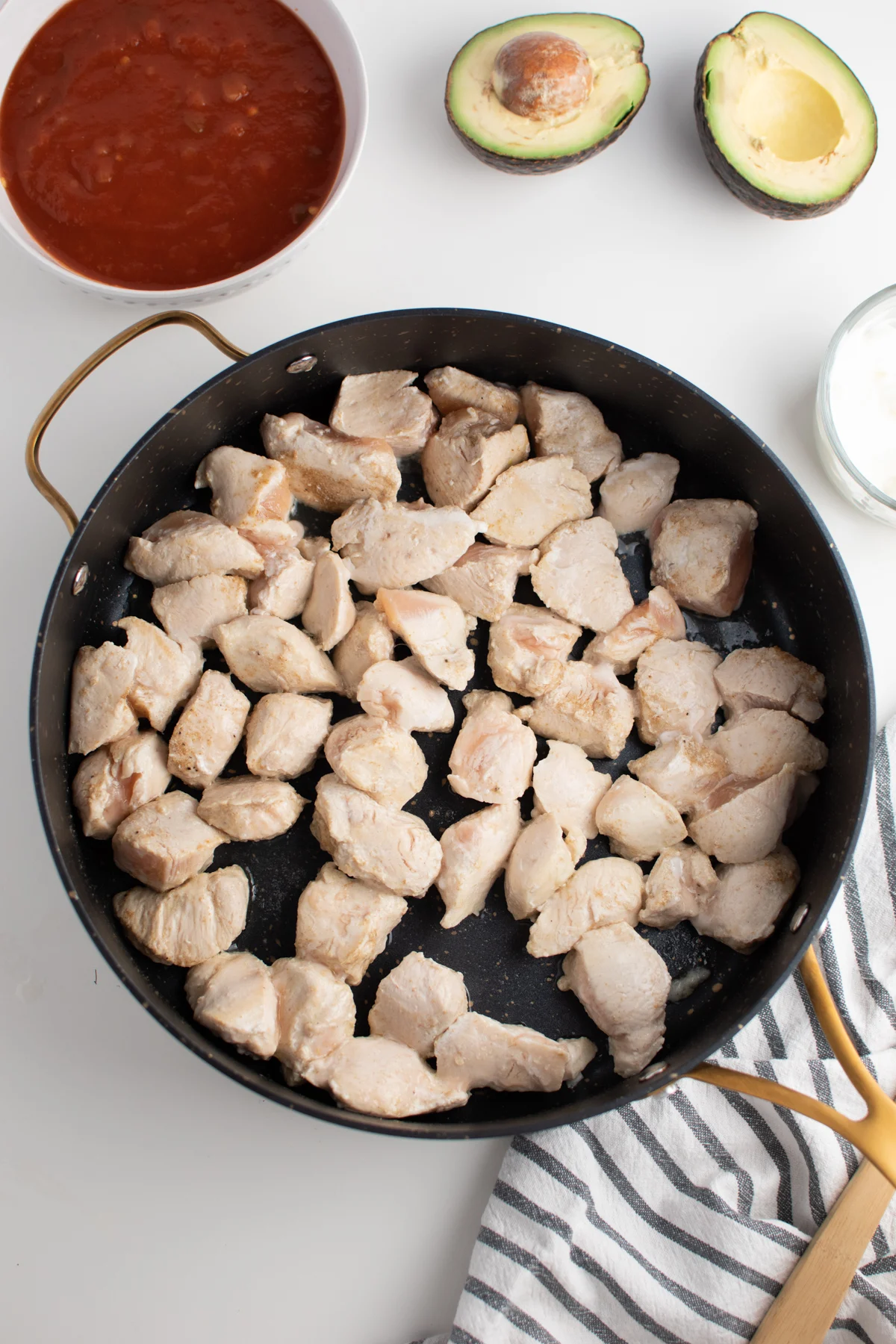 Cooked chicken pieces in large skillet next to bowl of picante sauce and avocado.