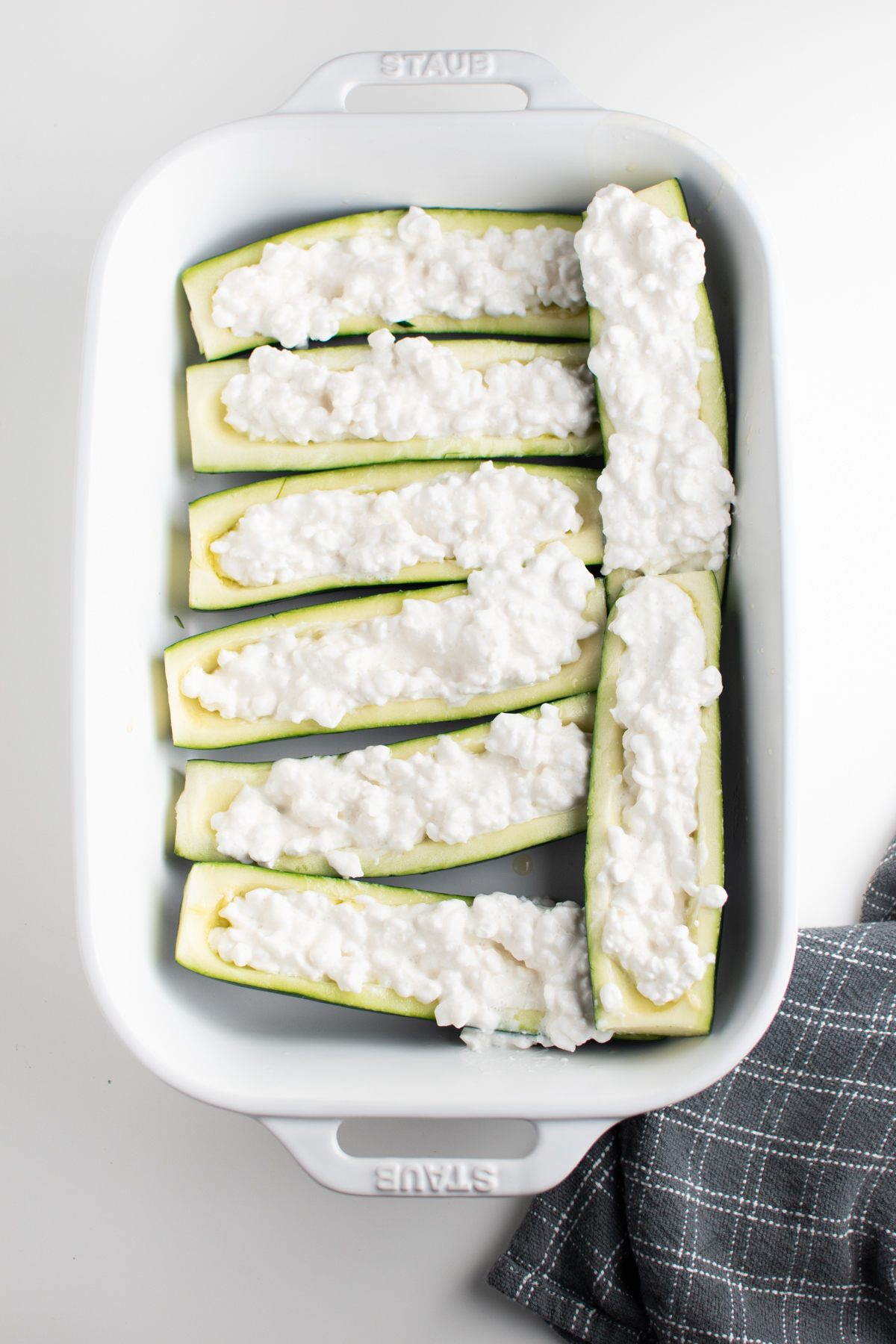 Cottage cheese filled zucchini boats in white baking dish on white table.