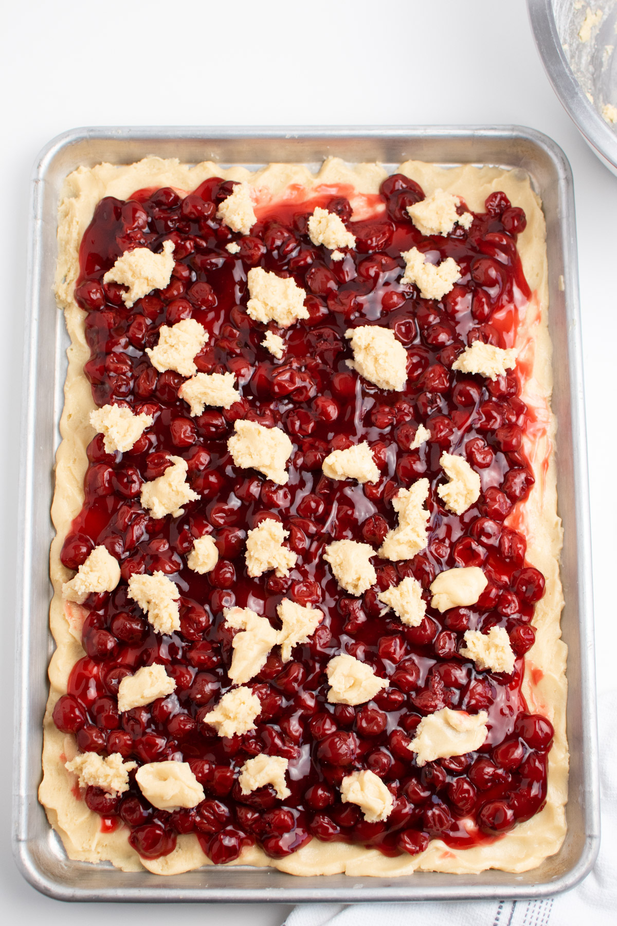 Dotted batter on cherry bars over crust on large metal making sheet.