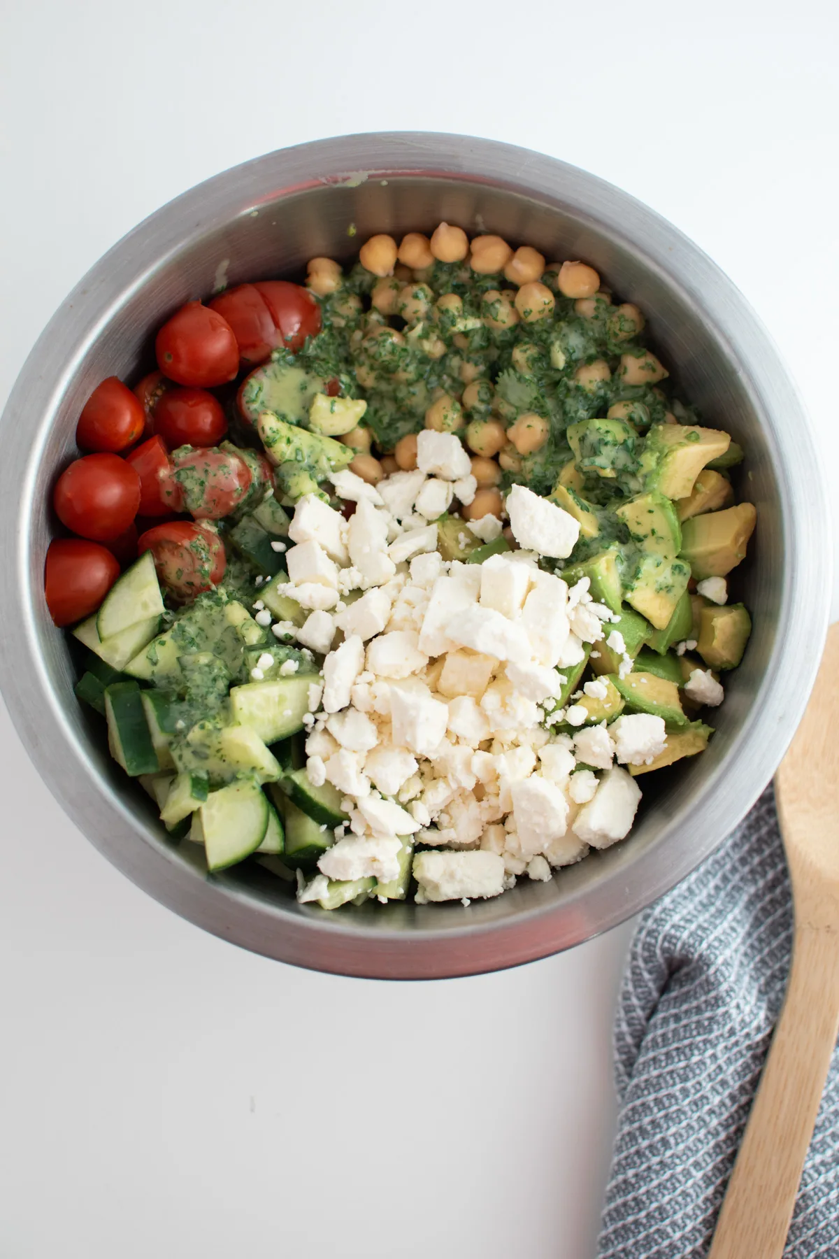 Feta cheese in chickpea salad with tomatoes, cucumber and avocado in mixing bowl.
