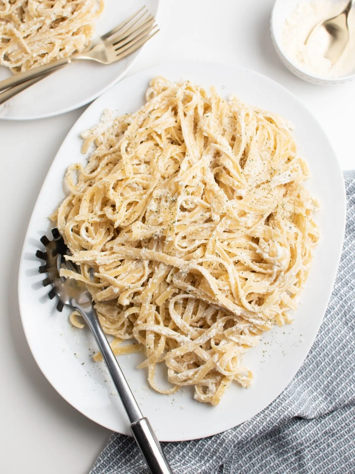 Large white platter with healthy fettuccine alfredo and pasta spoon and blue kitchen towel.