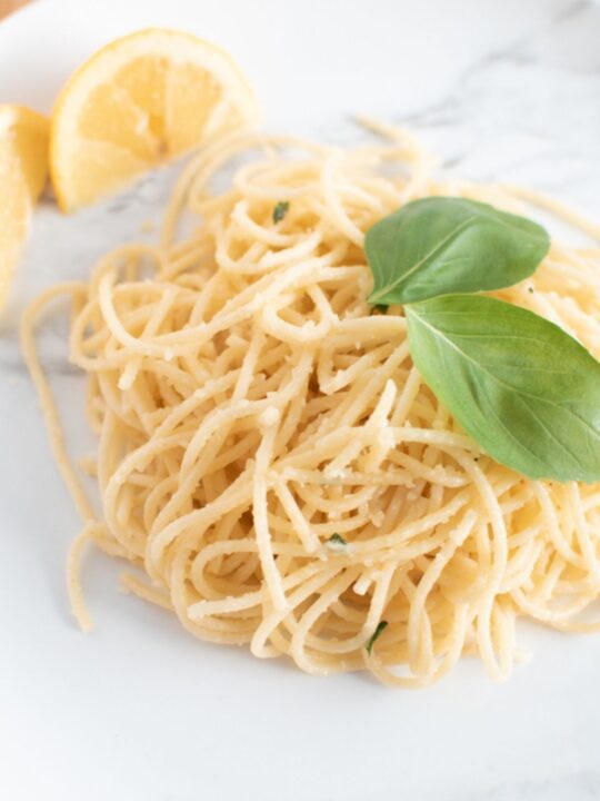 Garlic lemon basil pasta with bright green basil garnish next to slices of lemon.