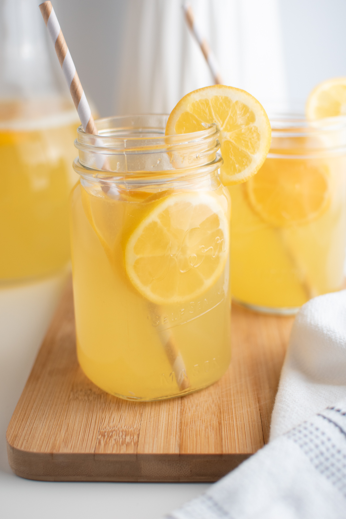 Glass cups of Meyer lemon lemonade on wood board with lemon garnish.