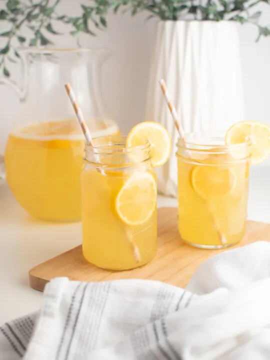Meyer lemonade in glass cups with striped straws on wooden cutting board.