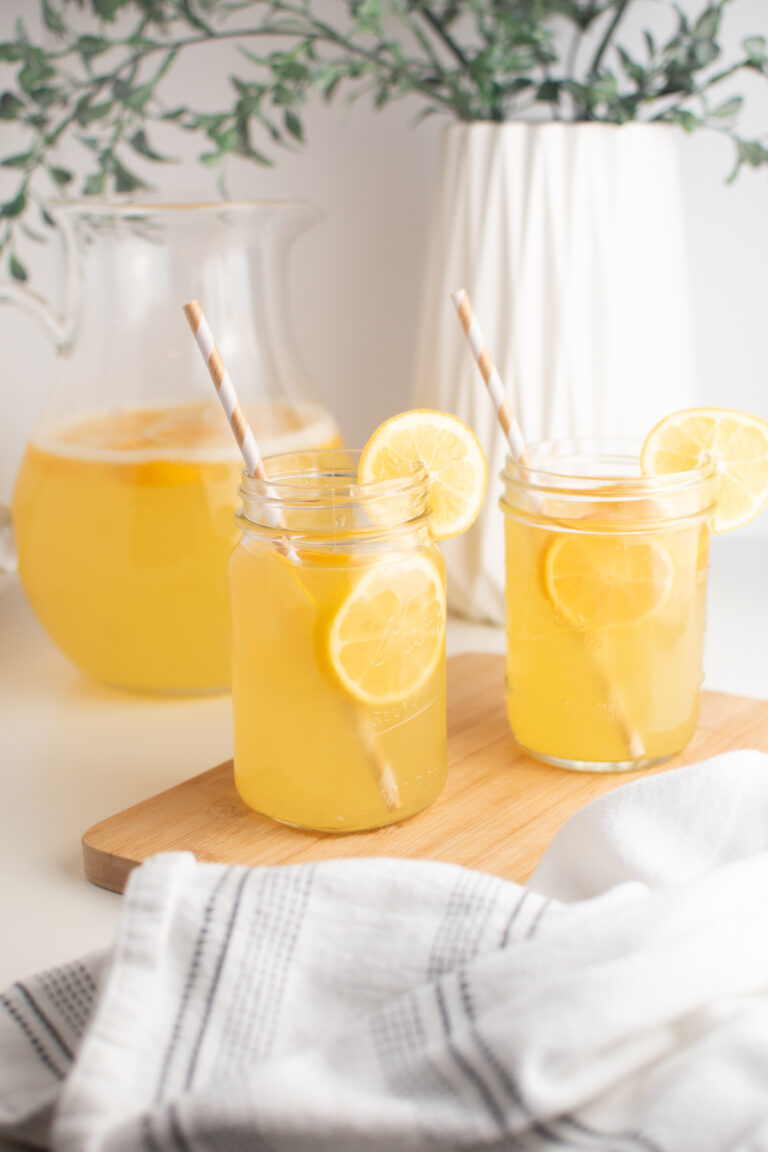 Meyer lemonade in glass cups with striped straws on wooden cutting board.
