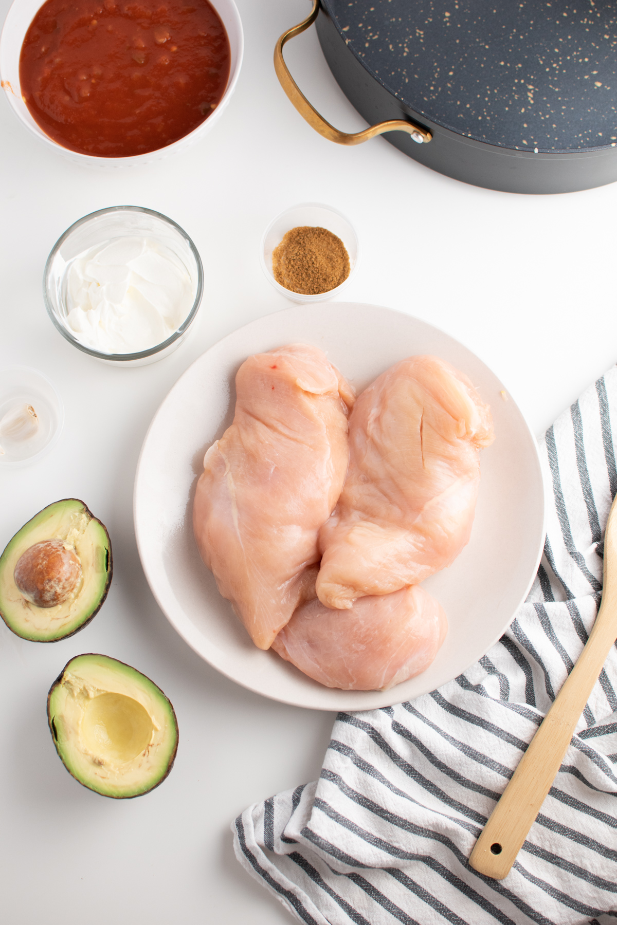 Picante chicken ingredients including raw chicken breast, avocado and seasonings by skillet.
