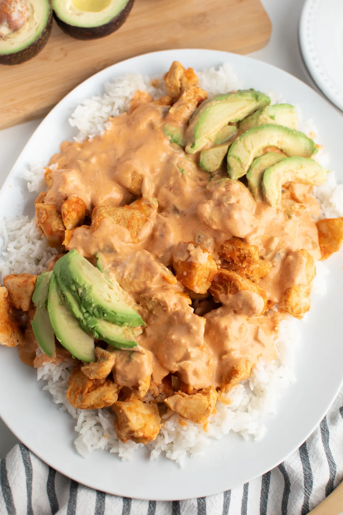 Picante chicken with avocado over rice next to cut avocado on cutting board.