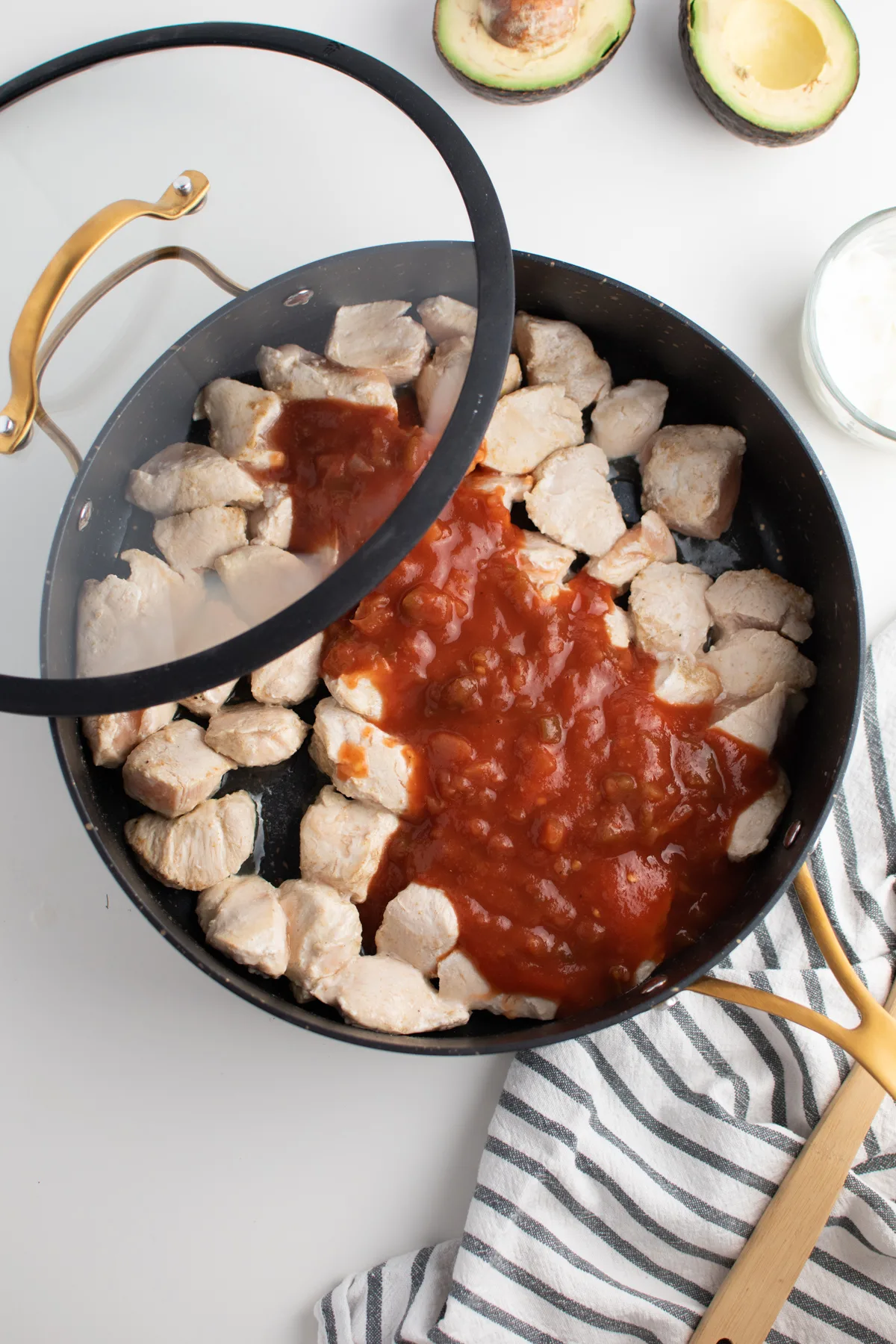 Picante sauce over cooked chicken pieces in large black skillet with lid.