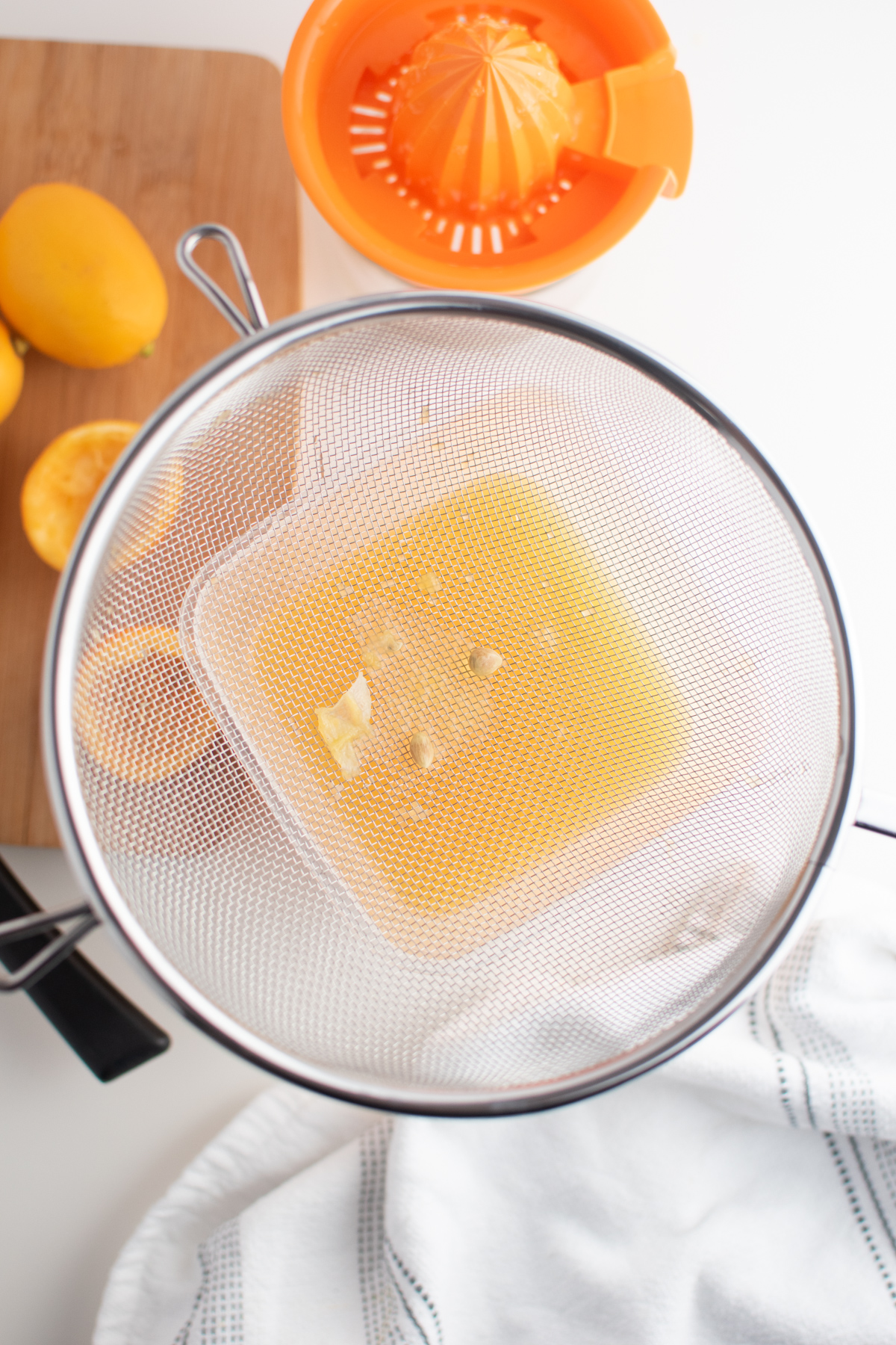 Strained lemon juice under fine mesh sieve next to juicer and wooden cutting board.