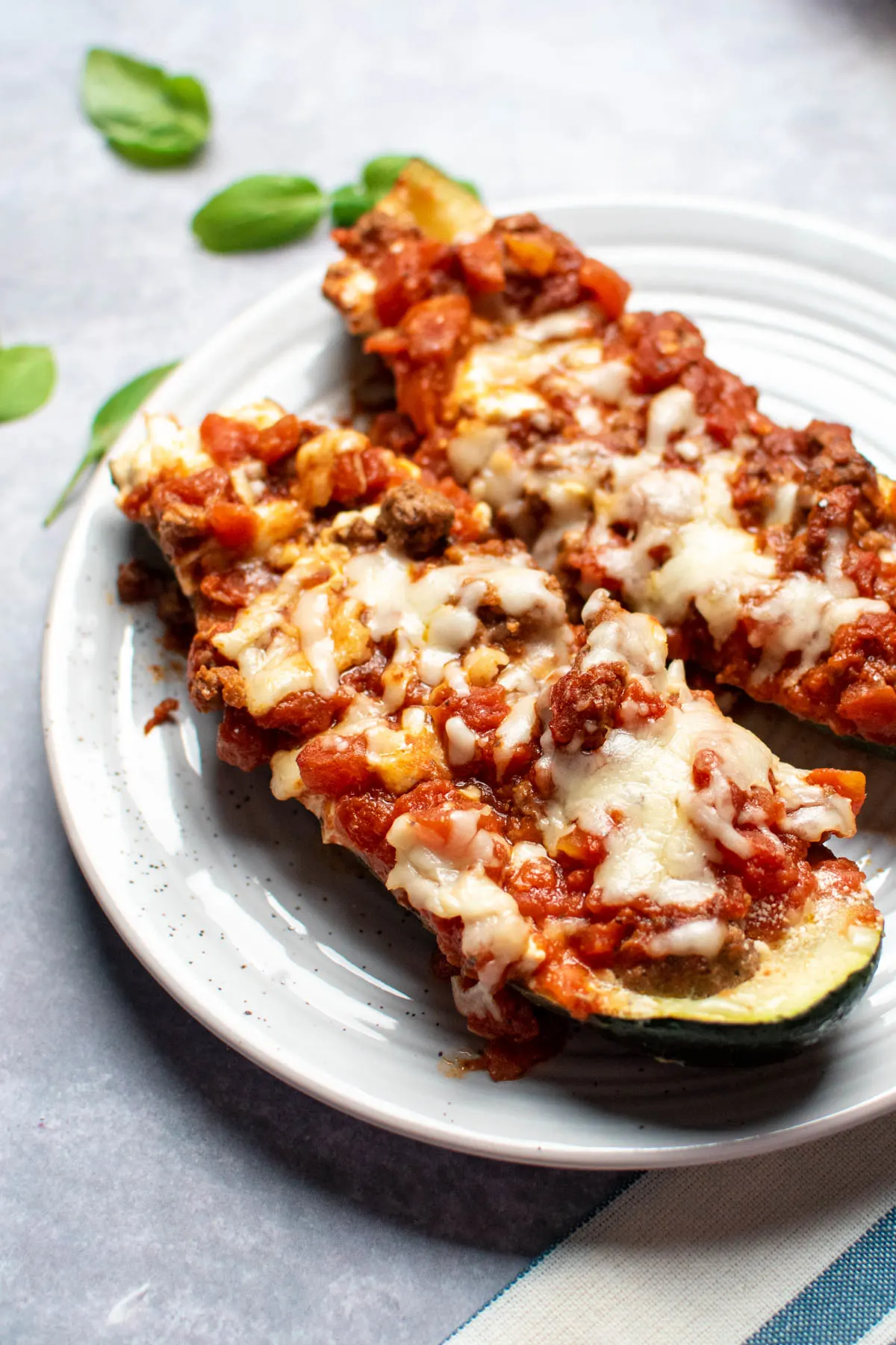 Two zucchini boats with ground beef, mozzarella, and tomatoes, on plate.