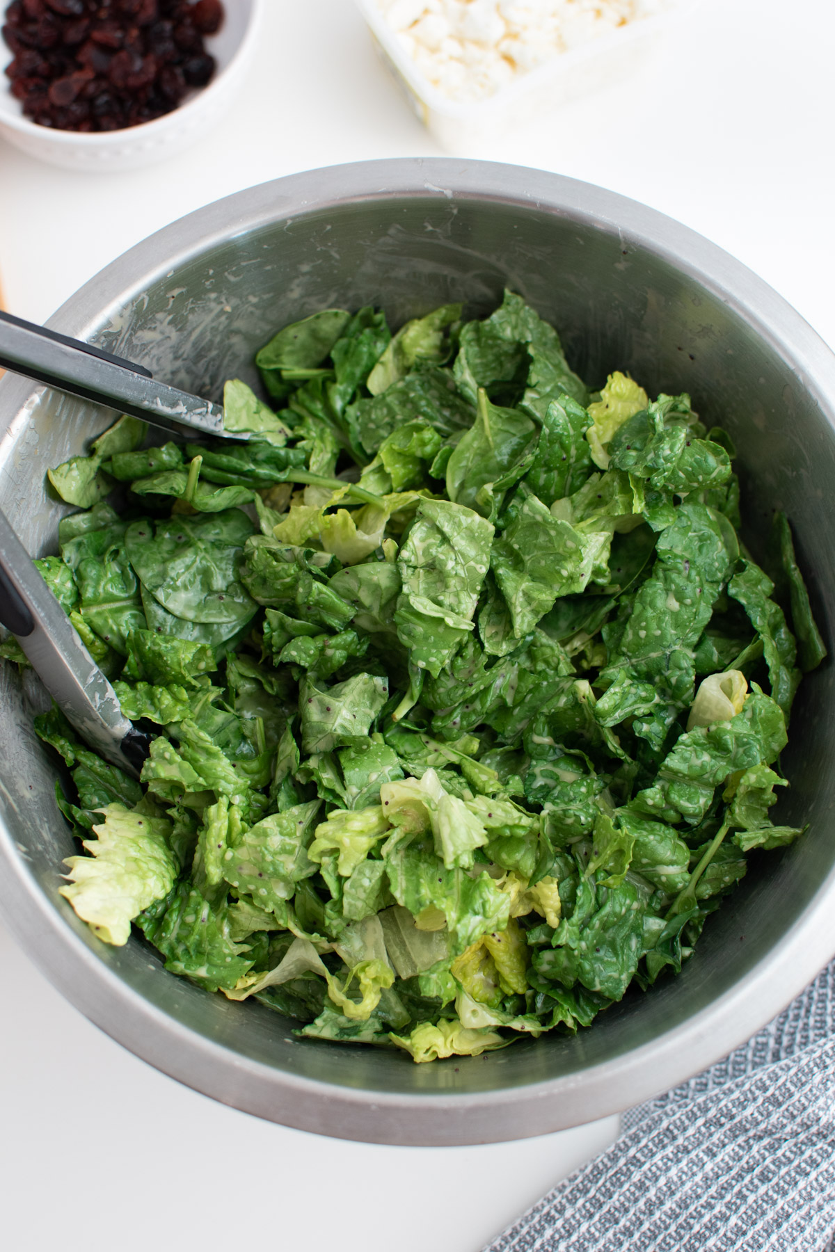 Lettuce and spinach covered in dressing in a large metal mixing bowl.