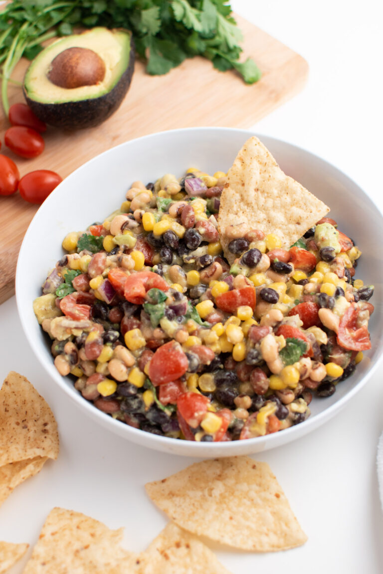 Bowl of cowboy caviar with tortilla chips next to cutting board with fresh veggies.