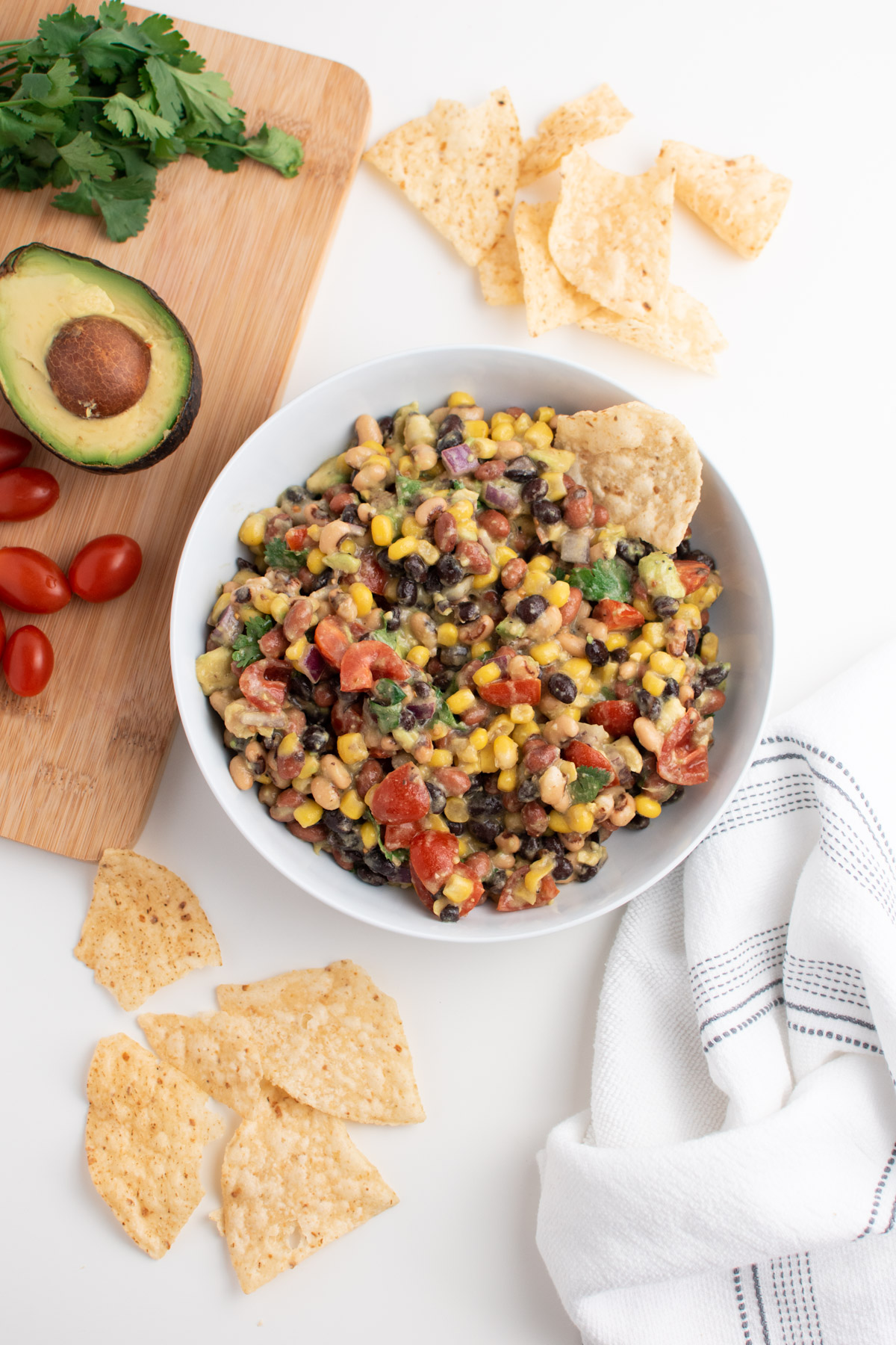 Cowboy caviar with italian dressing in white bowl next to cutting board and tortilla chips.