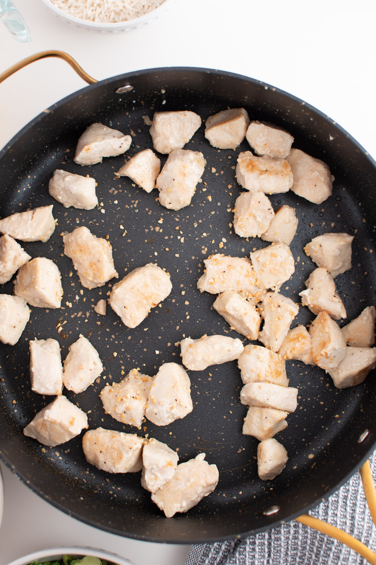 Minced garlic in large black skillet with browned chicken pieces.