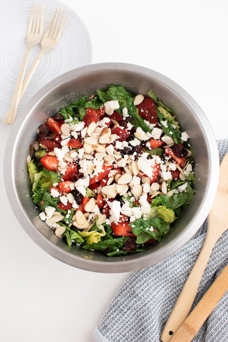 Spinach strawberry salad in large metal mixing bowl next to plate with forks.