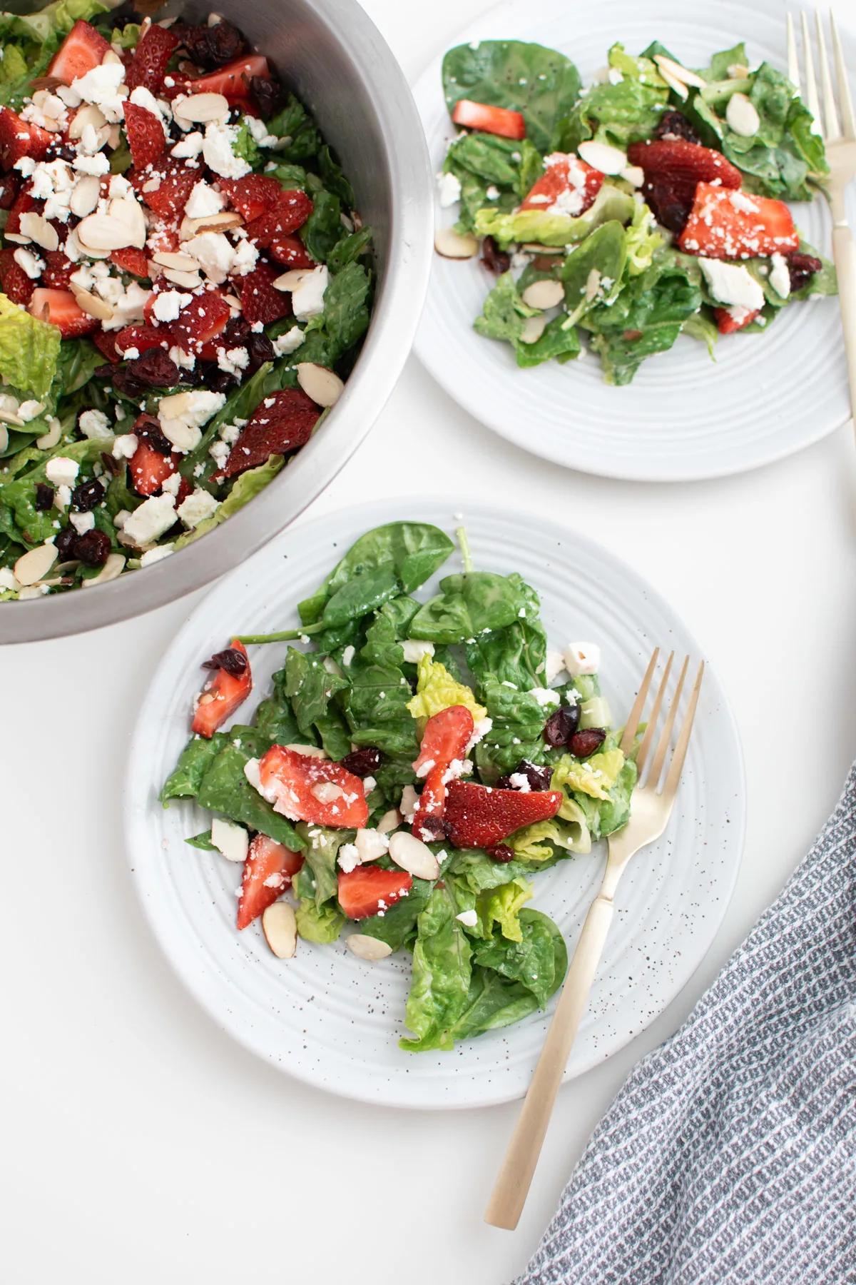 Two plates of spinach strawberry salad with almonds and feta next to salad bowl.