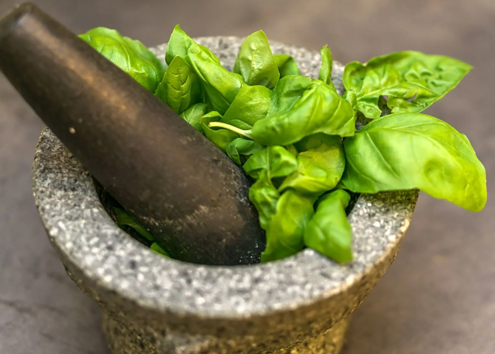 Close up of bright fresh green basil in small mortar and pestle.