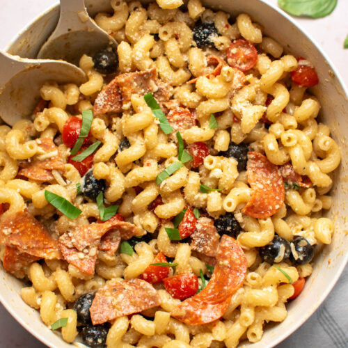 Pizza pasta salad with cavatappi, olives, pepperoni, and fresh basil in a large cream bowl.