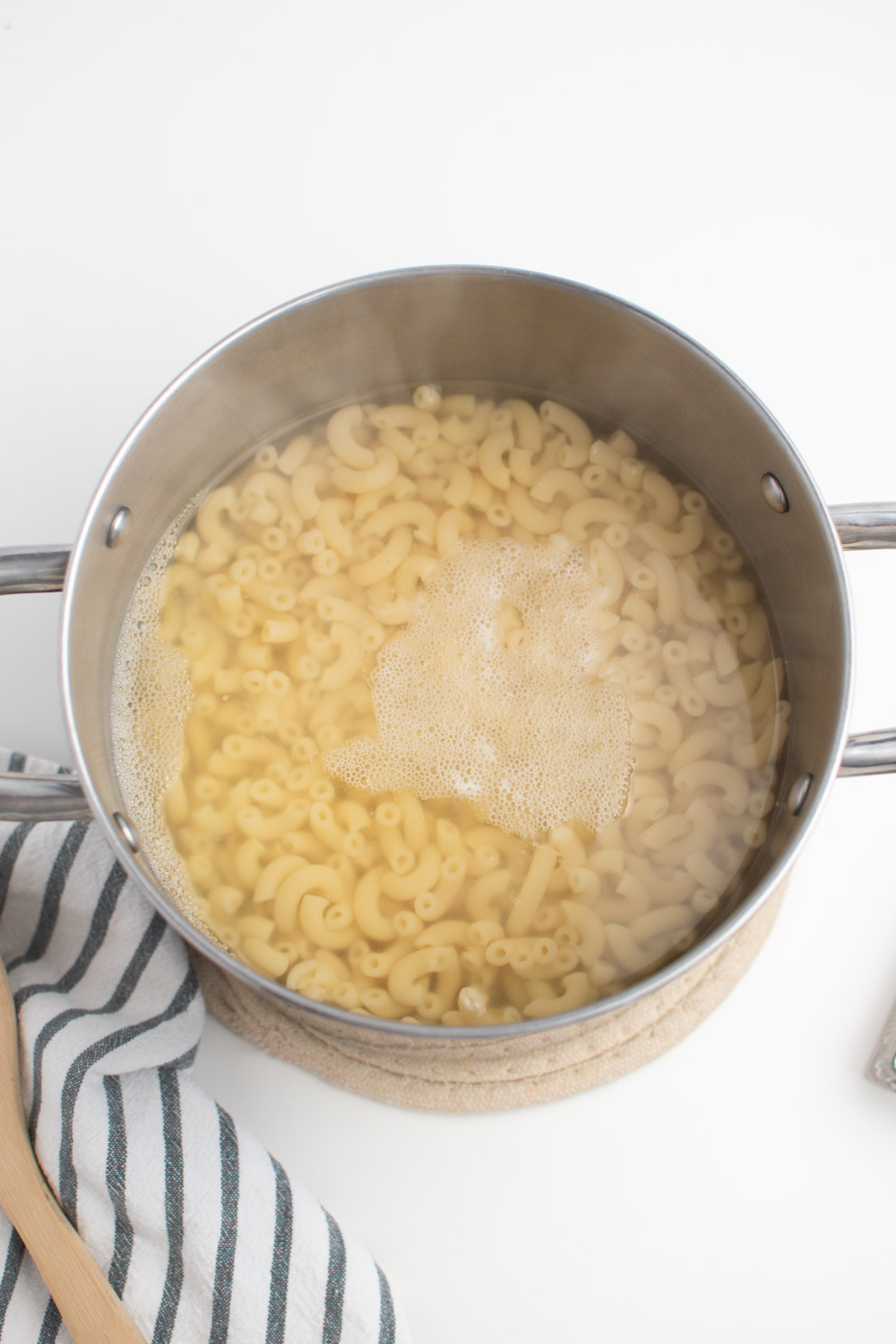 Cooked macaroni noodles and water in large metal pot on white table.