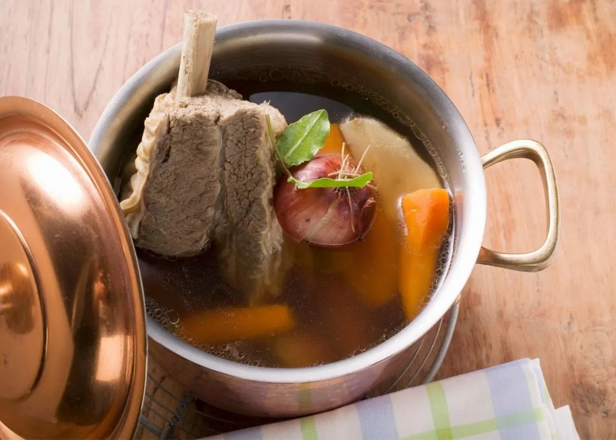 Homemade beef broth in small metal stock pot with carrots and aromatics.